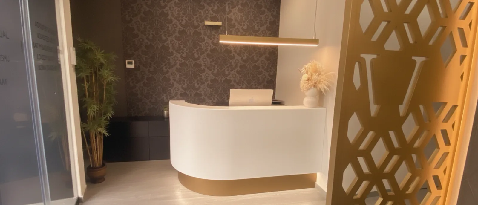 Recepció d’AURA Clinics, amb el taulell corb i la gelosia daurada