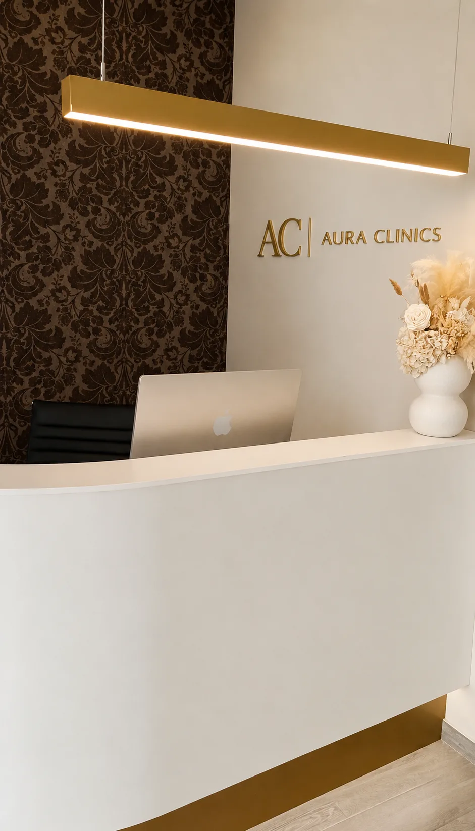 Taulell de recepció d’AURA Clinics, amb la lluminària daurada i les flors seques